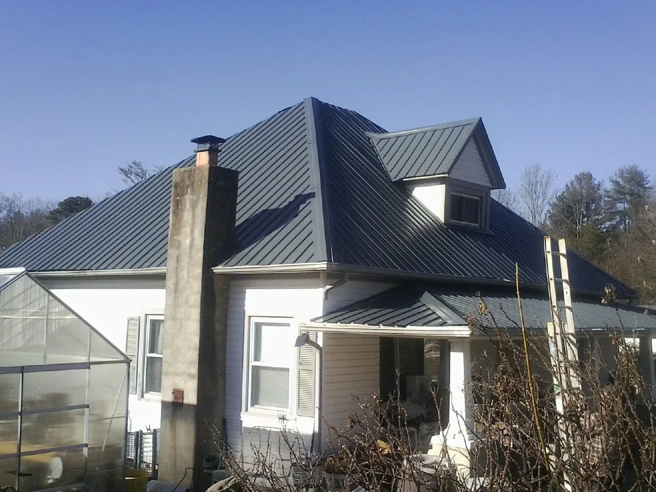 Dark blue standing seam metal roof on a white farmhouse with dormer — Slate & Tile Roof Repair by Roofing Brothers in Canehill