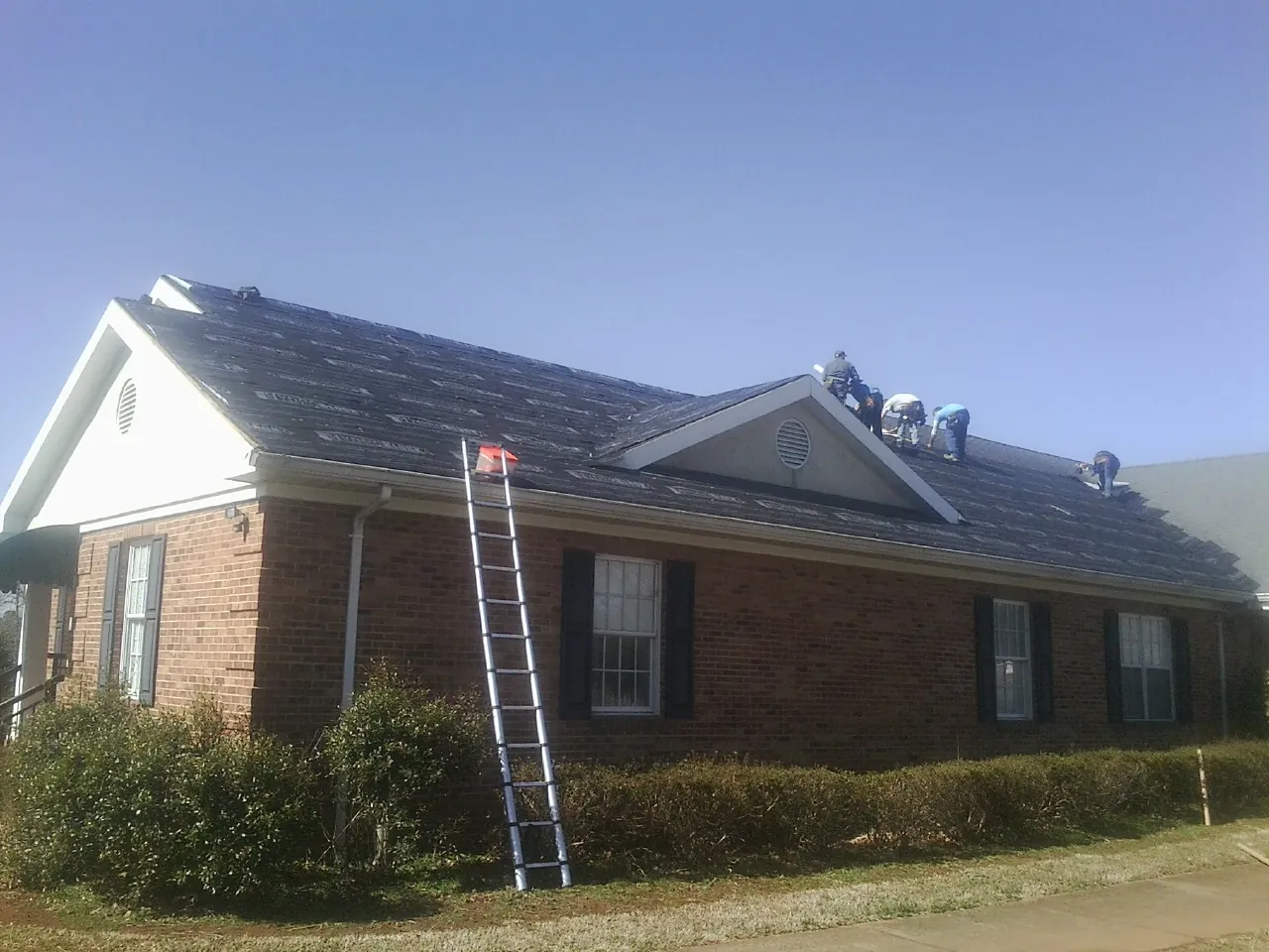 Crew tearing shingles off a brick ranch roof with a ladder set — Metal Roof Repair work by our crew in Canehill