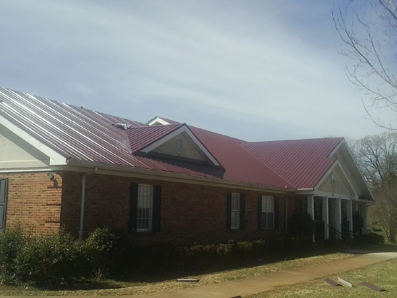 Red metal roof with gabled entries on a long brick building, from a Hail Damage Roof Repair job in Canehill