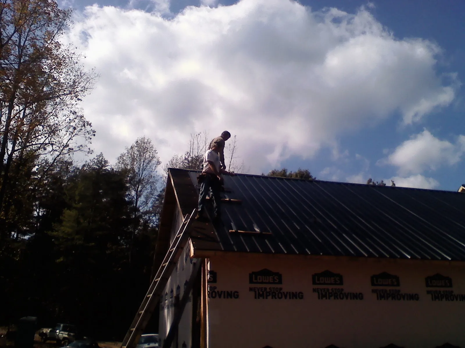 Roofer fastening dark metal panels high against a cloudy sky, from a Roof Inspection job in Canehill